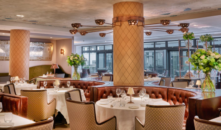 A photograph of Sartoria's dining room, showing booth tables and elegant place settings with flowers 