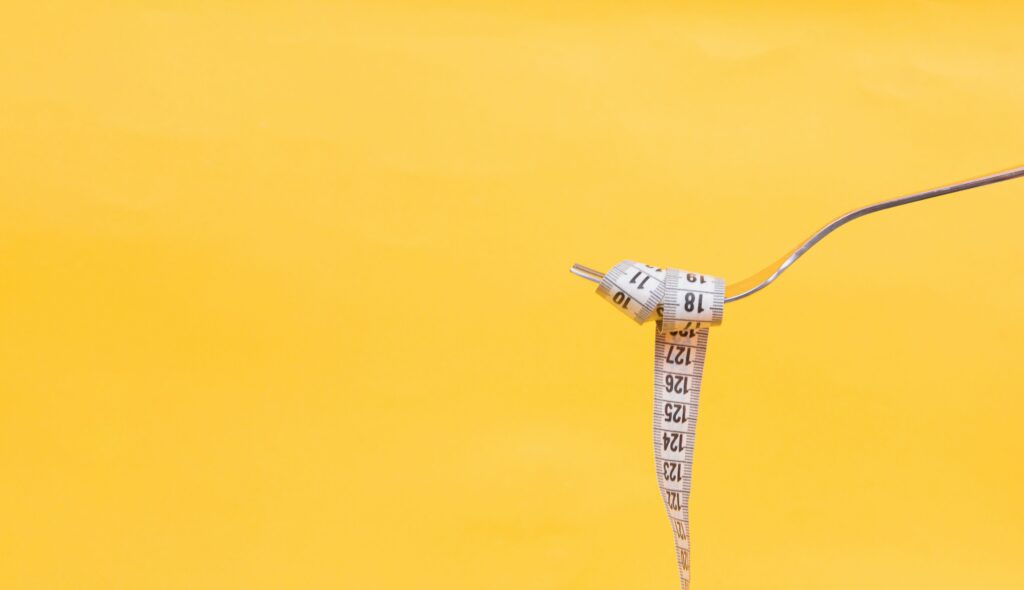 Female nutrition: image of a fork with a tape measure wrapped round it, yellow background. 