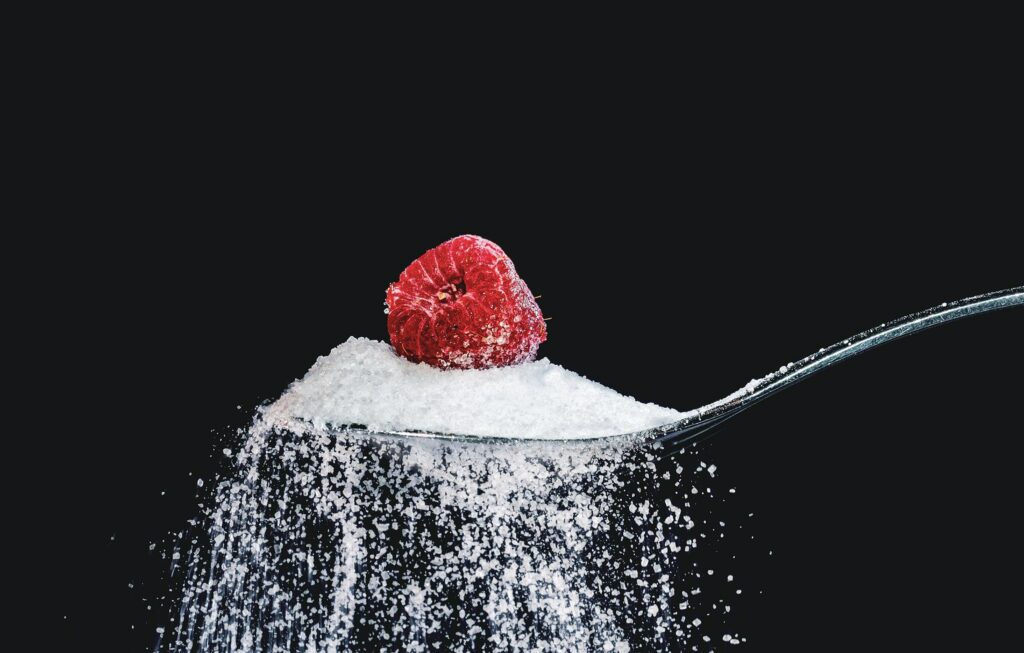 Spoon of sugar with a raspberry on top, black background.