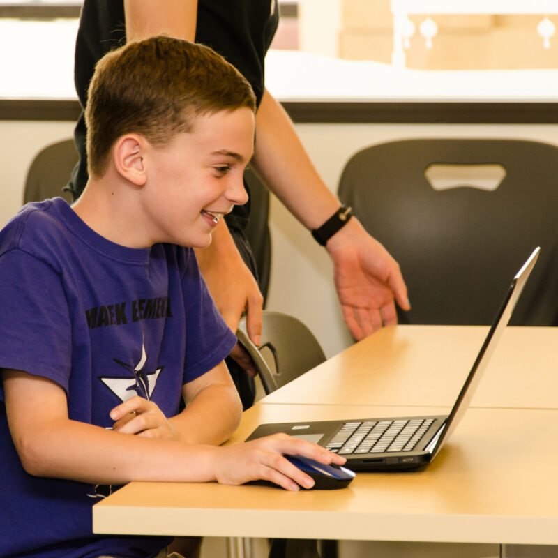 Boy smiling at laptop. AI has power to transform education.